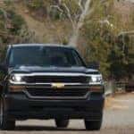 Black 2016 Chevrolet Silverado pickup truck parked on a dirt path in front of a brown gate