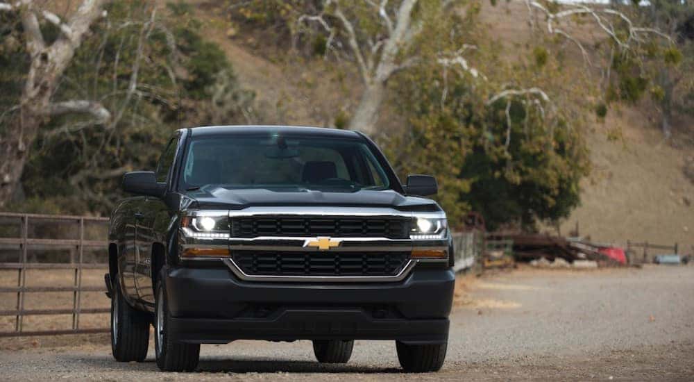 Black 2016 Chevrolet Silverado pickup truck parked on a dirt path in front of a brown gate