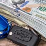 Blue toy car, car key, and a stack of one-hundred dollar bills sitting on a wooden surface