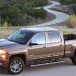 Brown 2015 Chevrolet Silverado pickup truck parked in front of grass, trees, and a long windy road