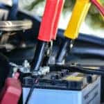 Car battery with jumper cables attached to it under the open hood of a vehicle
