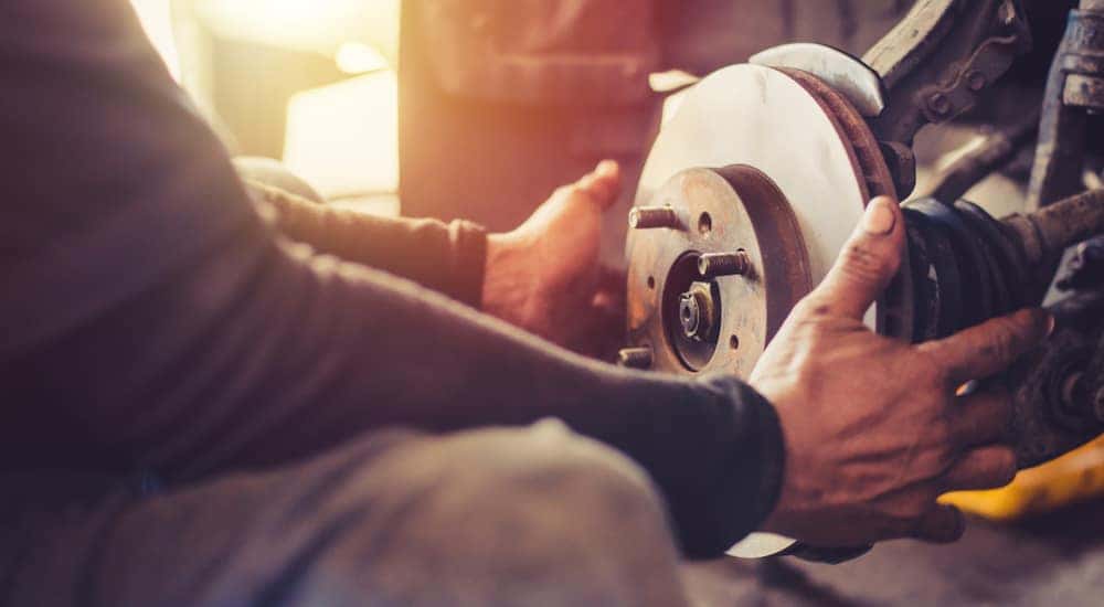 Mechanic in a black shirt and blue jeans working on the brakes of a vehicle