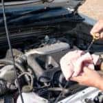 Person checking the oil under the open hood of a vehicle