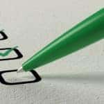 Black boxes on a white piece of paper with green check marks in them being drawn by a pen