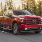 A red 2020 Chevy Silverado 1500 diesel is driving on a highway past evergreen trees.