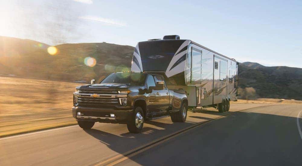 A black 2020 Chevy Silverado 3500 is towing a large camper on a highway.