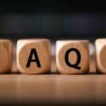 Brown wooden die with letters on them that spell out "FAQS" sitting on a brown table