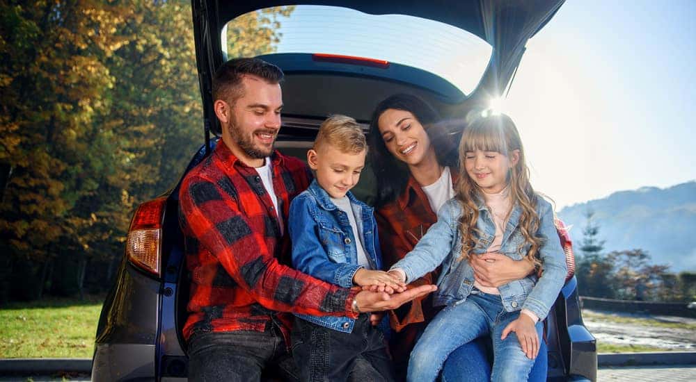 Mom and dad in plaid shirts holding a son and daughter in jean jackets while they sit in the open trunk of a vehicle