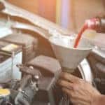 Mechanic pouring transmission fluid under the hood of vehicle through a grey funnel