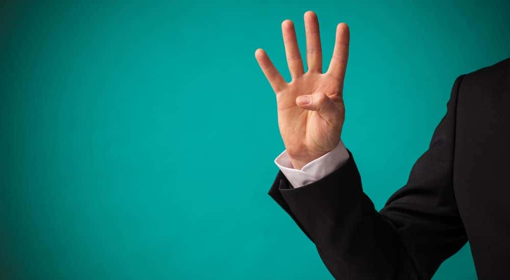 Hand of a man in a suit holding up four fingers in front of a blue-green wall