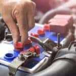 Man's hand working on a battery under the hood of a vehicle