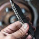 Hand holding a brake pad in front of a car wheel
