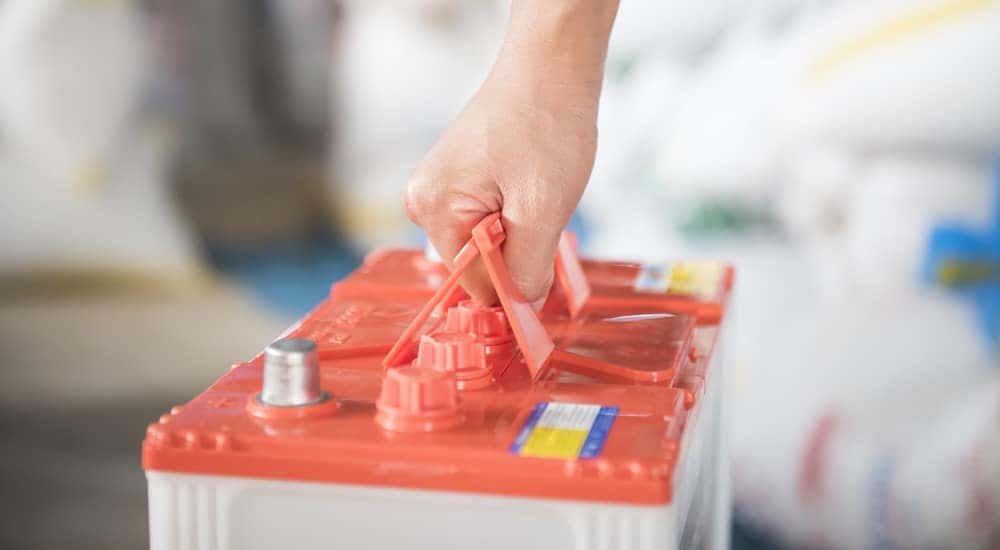 Hand holding handles on an orange and white car battery