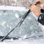 Hands pulling up windshield wipers off of the snowy windshield of a vehicle