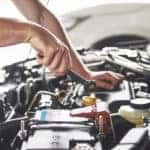 Man's hands working with tools under the open hood of a vehicle