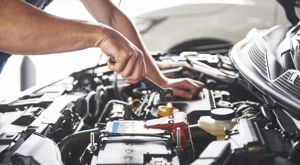 Side view of a man's hands working under the hood of a Chevy vehicle