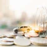 Jar of change on its side spilling change out of the top with a toy car sitting on top