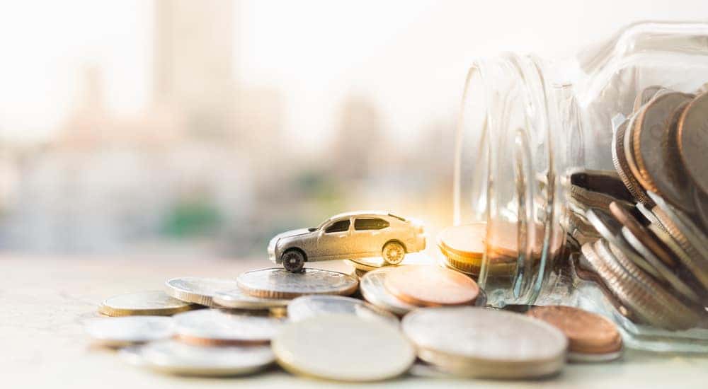 Toy car sitting on top of change that is spilling out of a glass jar