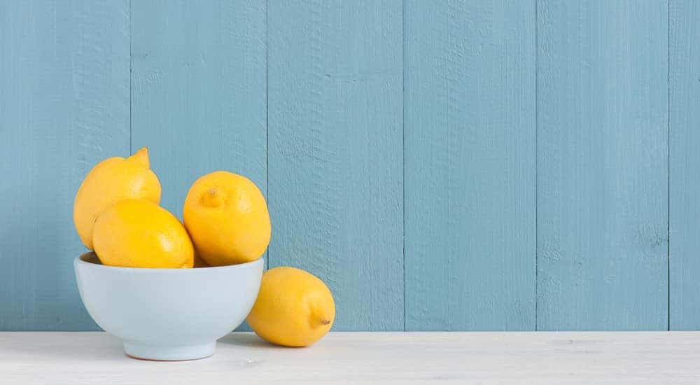 Lemons sitting in a white bowl in front of a blue wall