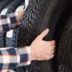 Man in a plaid button-up shirt grabbing a tire off of a shelf