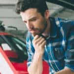 Man in a blue plaid shirt looking at a piece of paper next to cars