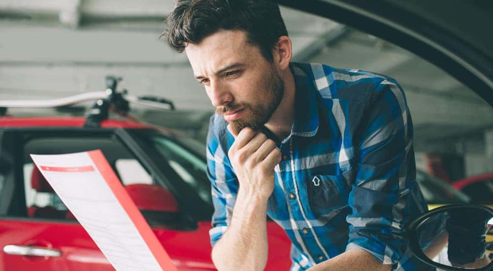 Man in a blue plaid shirt looking at a piece of paper next to cars