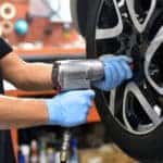 Mechanic in a black shirt and blue gloves changing a car tire with an electric drill