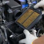 Man in white cotton gloves changing the air filter under the hood of a vehicle