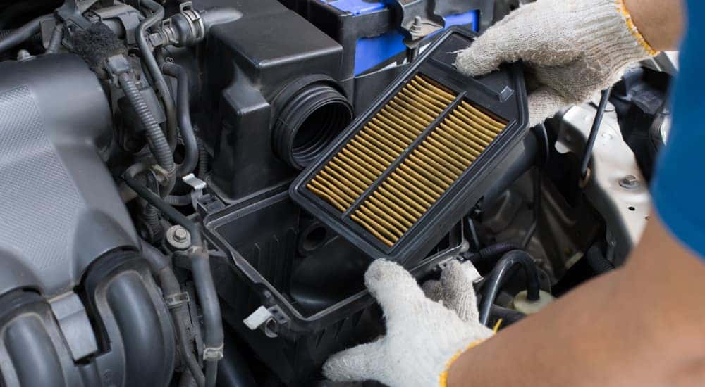Man in white cotton gloves changing the air filter under the hood of a vehicle