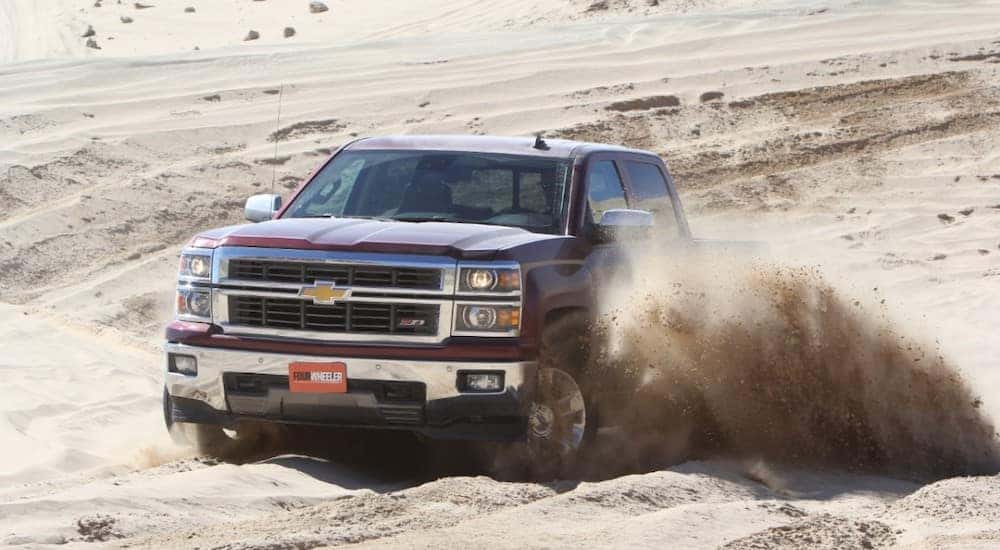 Maroon 2014 Chevrolet Silverado 1500 truck driving through the sand