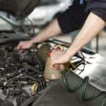 Mechanic in blue overalls leaning over the open hood of a vehicle