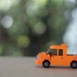 Orange toy truck on a table in front of a blurry green background