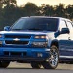 Blue 2011 Chevrolet Colorado parked on pavement in front of water and trees