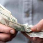 Man in a blue button-up shirt holding and counting cash