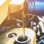 Oil being poured from a blue container into the tank under the hood of a vehicle