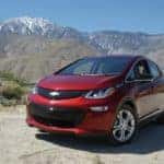 Red 2017 Chevrolet Bolt EV parked in a dirt lot in front of tall mountains