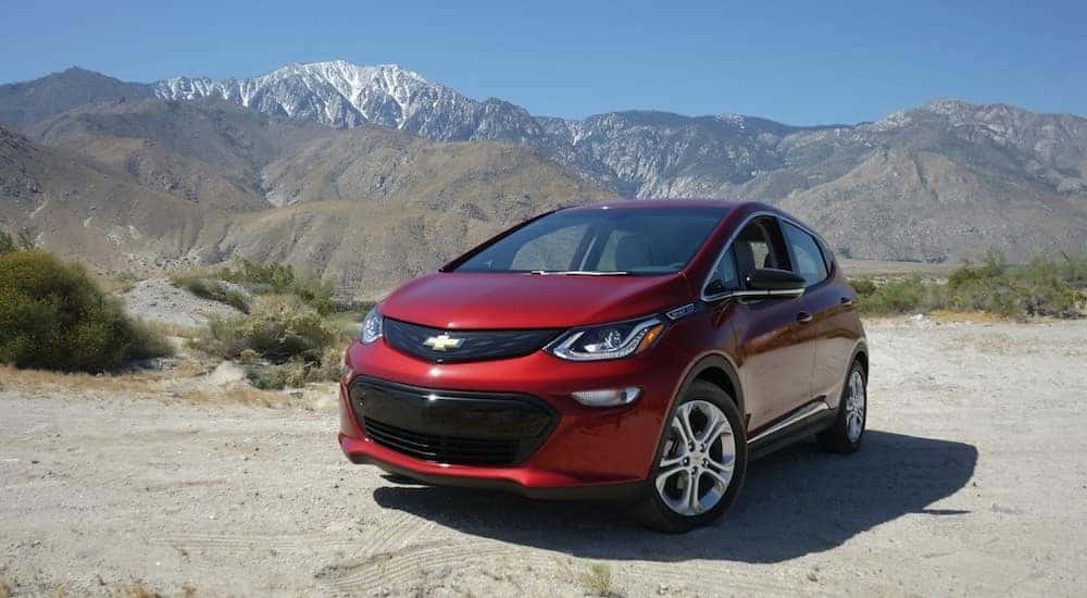 Red 2017 Chevrolet Bolt EV parked in a dirt lot in front of tall mountains