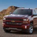 Red 2017 Chevrolet Silverado pickup truck parked across a paved road next to dirt hills