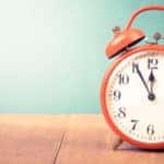 Red alarm clock sitting on a brown wooden surface in front of a light blue-green wall