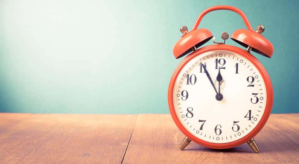 Red alarm clock sitting on a brown wooden surface in front of a light blue-green wall