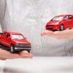 Hands holding a red toy hatchback vehicle and one red toy truck