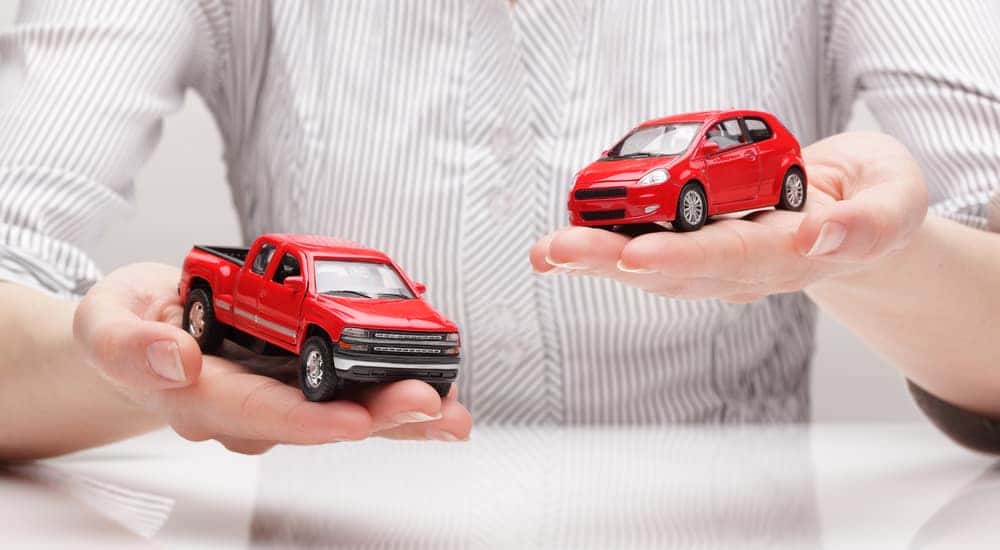 Hands holding a red toy hatchback vehicle and one red toy truck