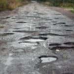 Long paved road with many water-filled potholes