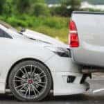 White sedan rear ending a grey pickup truck on a paved road