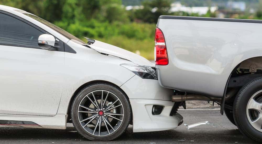 White sedan rear ending a grey pickup truck on a paved road