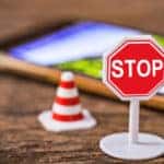 Plastic toy stop sign and traffic cone on a wooden table in front of a smartphone