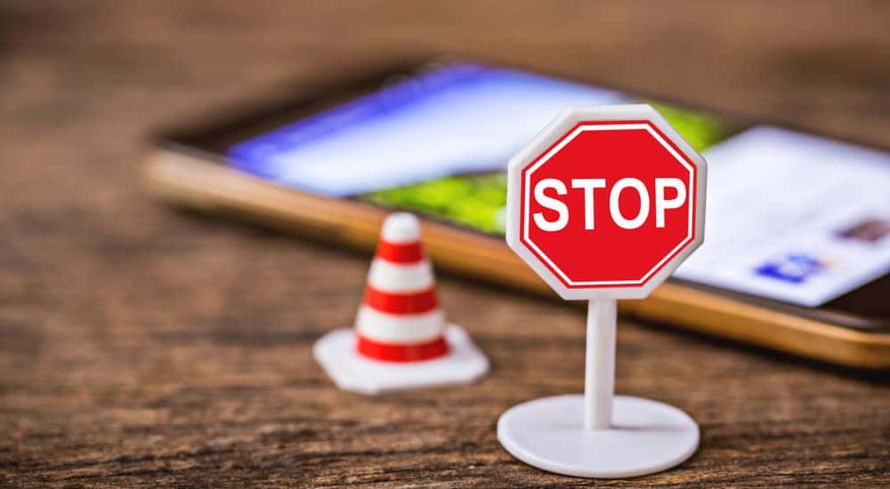 Plastic toy stop sign and traffic cone on a wooden table in front of a smartphone