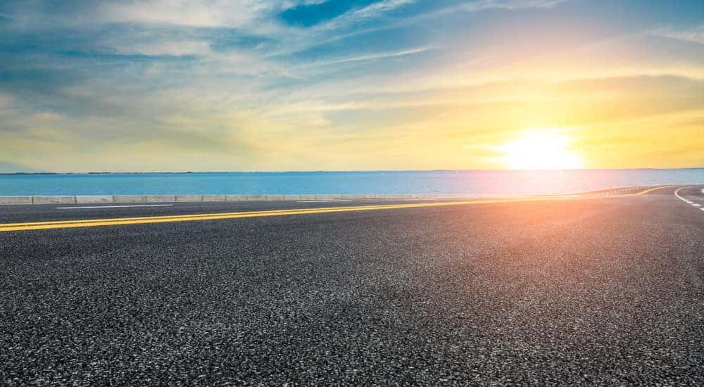 Paved road running alongside the ocean toward a summer sunset