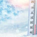White thermometer showing a low temperature and sitting in a pile of snow