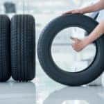 Man rolling a fourth tire toward a line of tires in front of a vehicle